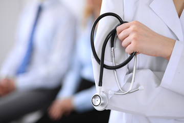 Doctor holding a stethoscope in his hands , the patient on the background