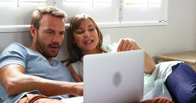 Happy couple lying on bed going shopping by internet