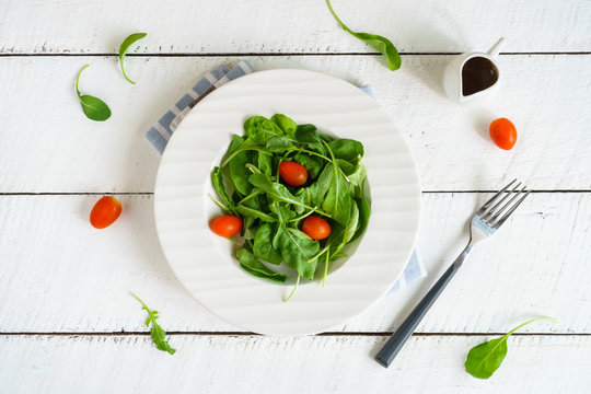 Rocket salad with cherry tomatoes on white wooden background