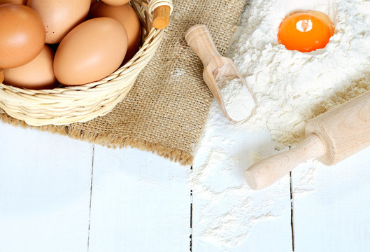 Eggs, flour, yolk, rolling pin and canvas bag on white wooden desk