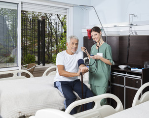 Naklejka premium Confident Nurse Checking Blood Pressure Of Patient In Rehab Cent