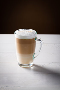 Original latte macchiato coffee in transparent glass on white wooden background.