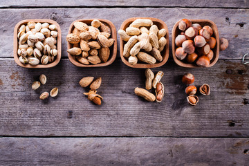 Hazelnuts, pistachios, peanuts and almonds on wooden bowls.