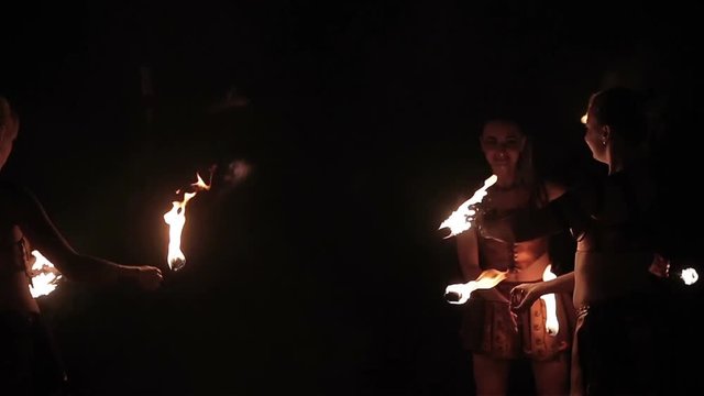 Fire show performance or dance competition. Group of sports women – female fire performers dance gathering up burning fire torches and stand in final move on black background. Slow motion