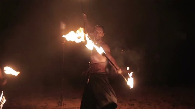 Fire show performance. Three handsome male fire performers twirling two fire batons staff ignited from both sides each. Slow motion