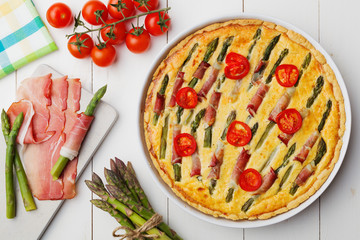 Tart with asparagus and tomatoes on white wooden background.