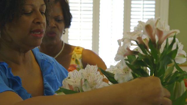 Scene tilts up past lilies and freesia to two lovely African American working on arranging the fresh flowers.