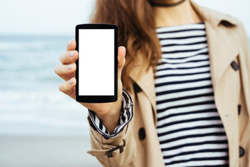 Girl in beige coat and striped t-shirt shows a blank screen phon