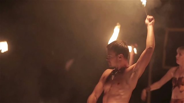Fire show performance. Group of fire show performers dance twirling fire snakes around on black background. Close-up. Slow motion