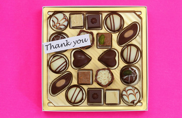 Thank you card with box of assorted chocolates on pink surface
