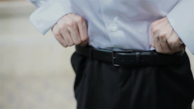 Man hands tighten trendy leather belt for his black trousers on his waist going to work official clothes look. Close-up