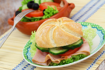 Lunch consisting of ham roll with lettuce, tomato and cucumber and bowl of green side salad
