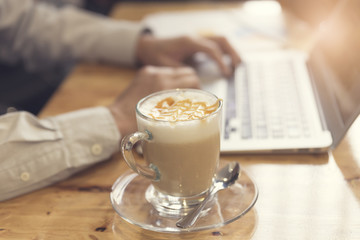 man's hand working with laptop computer with cup of hot latte co