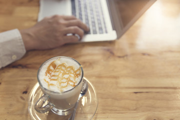 man's hand working with laptop computer with cup of hot latte co