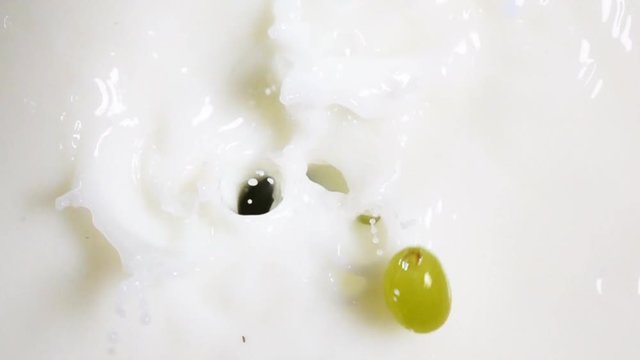 Berries of grape fall into the fresh white milk in slow motion. Shot on high-speed camera Sony RX 10 ii