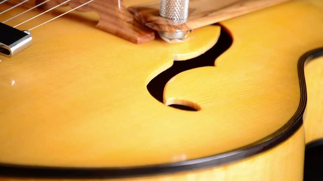 Detail of bridge, strings and efes of a jazz electric guitar gyrating at black background