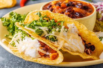Tacos with chili con carne, salad, cheese and sour cream.