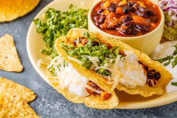 Tacos with chili con carne, salad, cheese and sour cream.