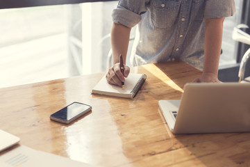 woman's hand writing on notebook with laptop computer, selective
