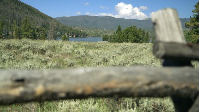 Focus moves from post of an old split rail fence to a mountain lake in rugged territory of the North American west.