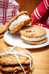 A couple of homemade ice cream sandwiches made out of two oatmeal and raisins cookies and chocolate chip ice cream in the middle, in a rustic kitchen