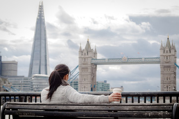 Woman having a cup of coffee in front of the Tower Bridge, in London, England, UK