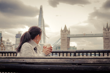 Woman having a cup of coffee in front of the Tower Bridge, in London, England, UK