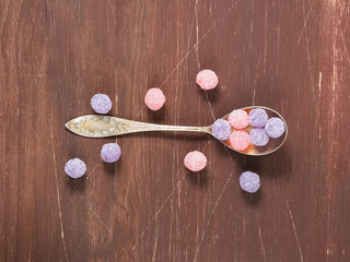 Round purple and pink candies in a vintage silver tea spoon on wooden background, top view