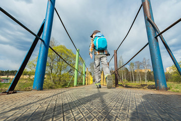 Small boy with backpack walking on the bridge.