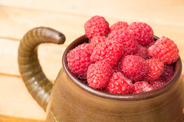 Fresh sweet raspberries in bowl on wooden table, summer raspberries