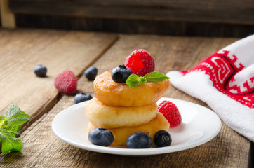 Cottage cheese pancakes with raspberries, blueberries and mint leaf, homemade traditional Ukrainian and Russian syrniki on rustic wooden background.