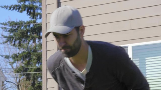Attractive Mediterranean Man in baseball cap and beard mows a backyard lawn with a push mower in close up