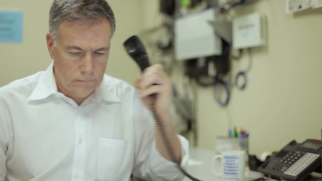 An network administrator sitting in his rather industrial looking office take a phone call on his desk phone.