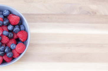 Dessert fresh berries in the bowl. Raspberries and blueberries on a wooden table. Dessert, fresh berries close-up.