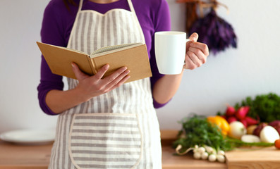 Young woman reading cookbook in the kitchen, looking for recipe