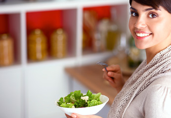 Young woman eating fresh salad in modern kitchen