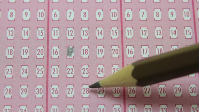 Pencil filling in numbered squares on lottery game piece.