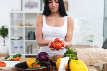 Girl standing at kitchen holding red tomato bunch in her hands. Housewife taking fresh ingredients for vegetable salad.