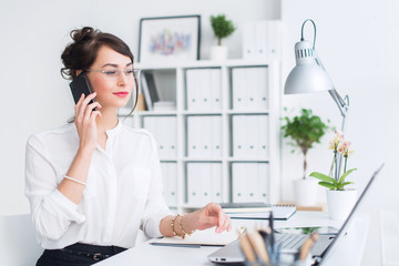 Beautiful female assistant calling using cellphone. Young office worker speaking on the mobile...