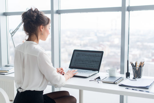 Young businesswoman working in office, typing, using computer. Concentrated woman searching information online, rear view portrait.