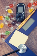 Electronic bathroom scale, glucometer, stethoscope and centimeter with colorful candies, diabetes, slimming and reduction eating sweets