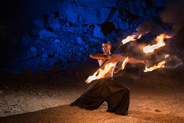 Fototapeta premium Fireshow performance in the desert near the rock illuminated with blue. Motions are blurred