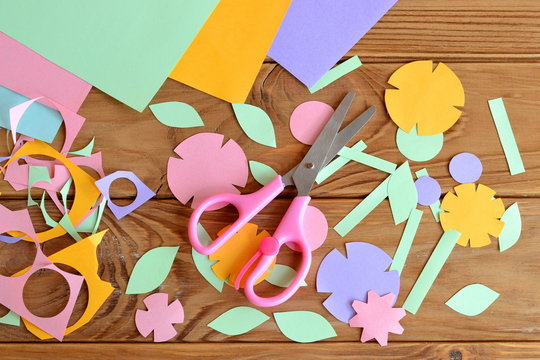Paper flowers, paper sheets, scissors, 
paper scrap on a wooden table. Paper flower craft for kids. Children's art project.