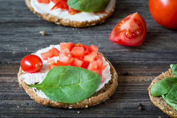 Healthy light snack toast with white cheese, tomato and baby spinach on rustic wooden backdrop. Selective focus, close up