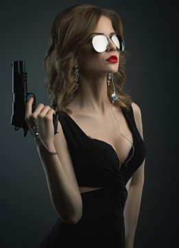 Sexy young woman in mirror sun glass holding gun studio shot