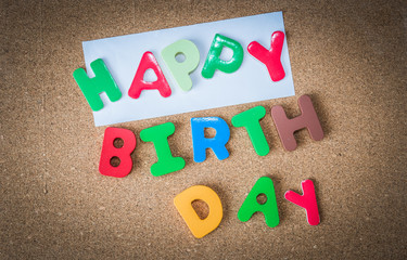 Colorful Wooden word HAPPY BIRTH DAY with piece of White paper on cork board