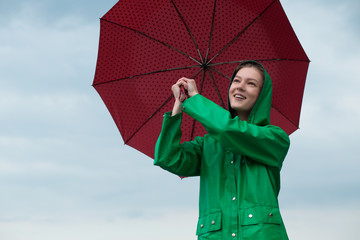 Woman in raincoat holding umbrella at overcast sky background
