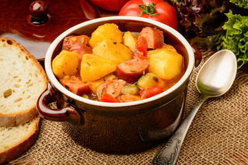 Vegetables stewed with pork sausages in ceramic pot.