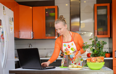 Woman grate carrots in the kitchen, with notebook.