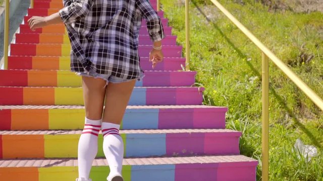 Young exotic woman in clothing jumping up the colorful stairs.